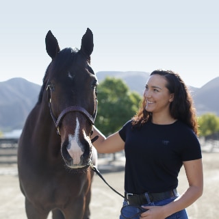 Girl standing next to a horse and looking at it.