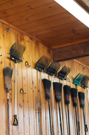 A wall with pitchforks and brooms neatly hung on it.